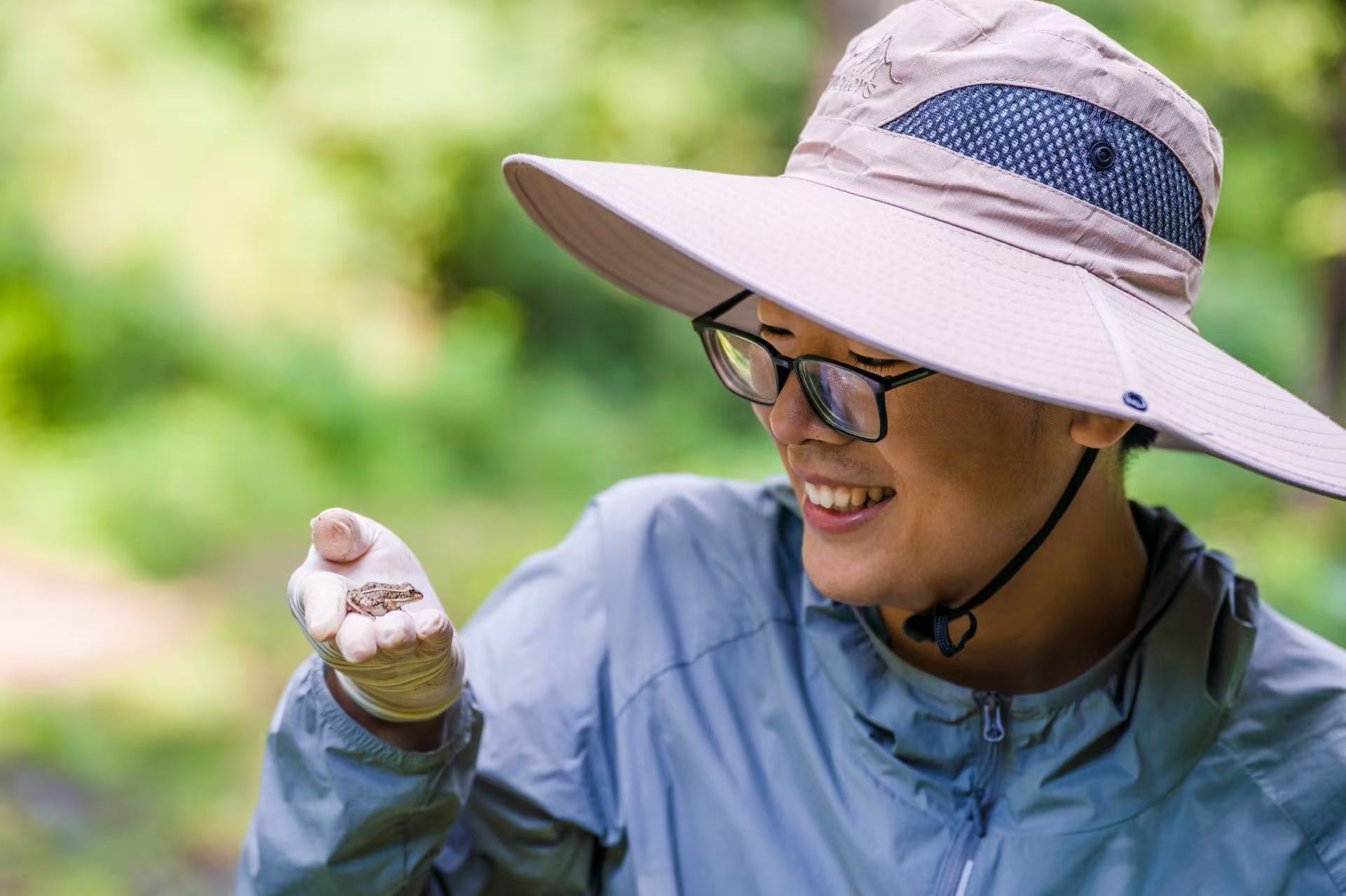 Yanchang Bian observing a small frog resting on his gloved hand outdoors